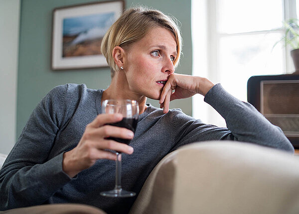 Eine Frau sitzt zu Hause auf dem Sofa und hält ein Glas Rotwein. Sie sieht deprimiert aus.