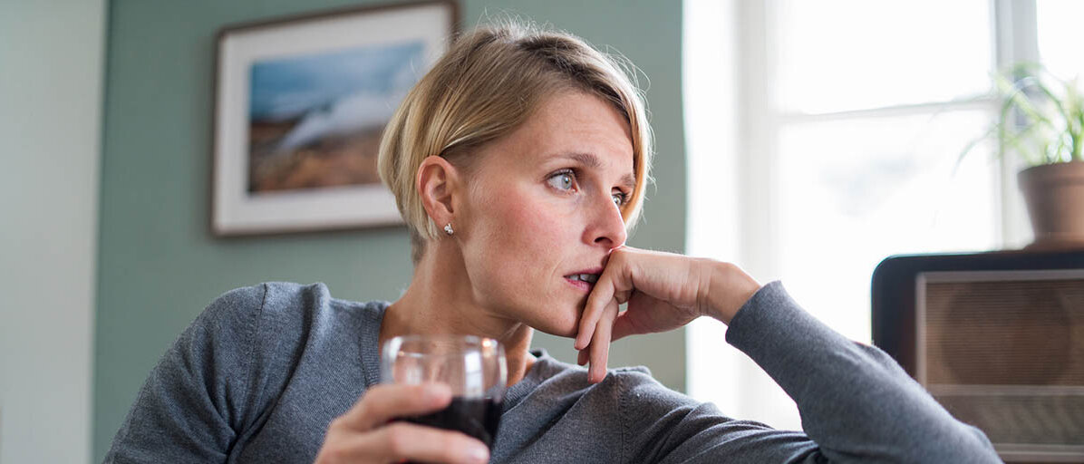 Eine Frau sitzt zu Hause auf dem Sofa und hält ein Glas Rotwein. Sie sieht deprimiert aus.