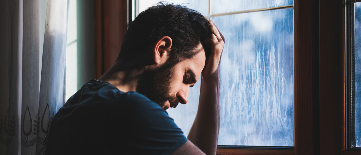 Mann sitzt traurig am Fenster
