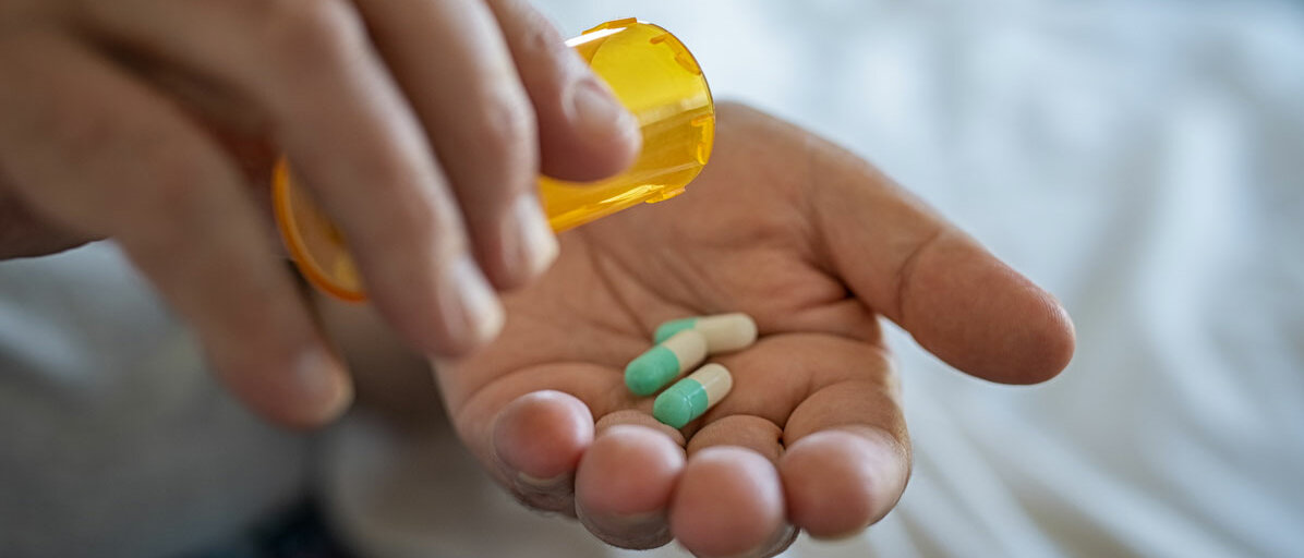 Frau kippt aus gelber Dose Tabletten in ihrer Hand