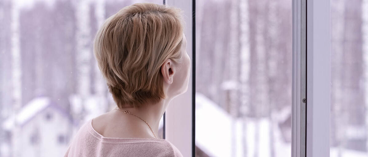 Hormonfreies Präparat: NK3-Rezeptorantagonist bei Hitzewallungen in den Wechseljahren Eine Frau schaut aus dem offenen Fenster. Draußen liegt Schnee.