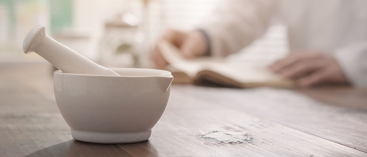 Mörser und Stößel auf einem Tisch im Hintergrund Person in Kittel