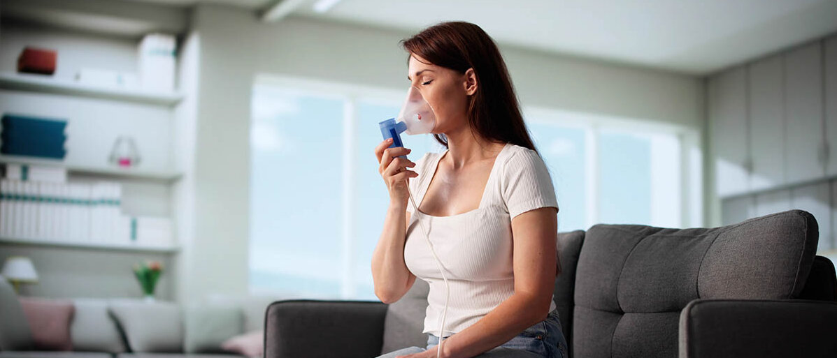 ErnĂ€hrung bei COPD: Proteine und Calcium sind wichtig. Tipps fĂŒr das Essen mit Luftnot. Eine junge Frau sitzt auf dem Sofa und inhaliert mit einem elektrischen Intervallvernebler.