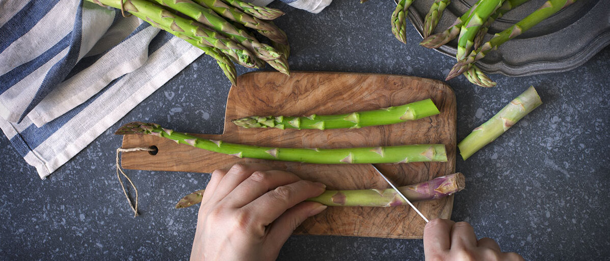 Frau bereitet frischen grünen Spargel auf einem Holzfrett zu