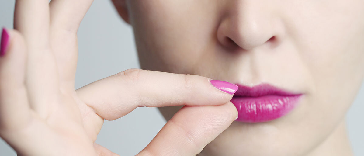 Frau mit rosa Lippenstift hält Finger an die Lippen