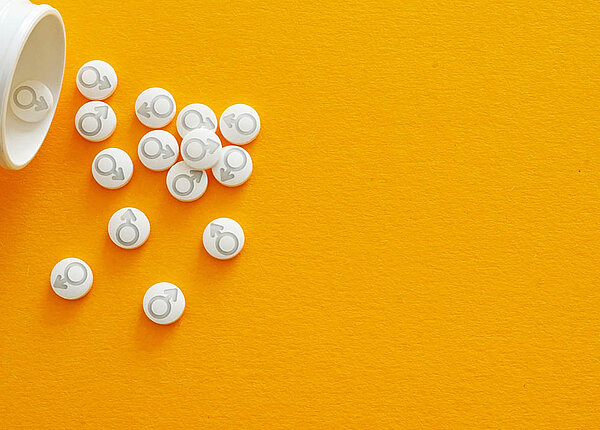 Eine offene Tablettendose, aus der Tabletten herauskullern: Sie sind mit dem Männlichkeitssymbol geprägt (Kriegsgott Mars, Kreis und Pfeil).
