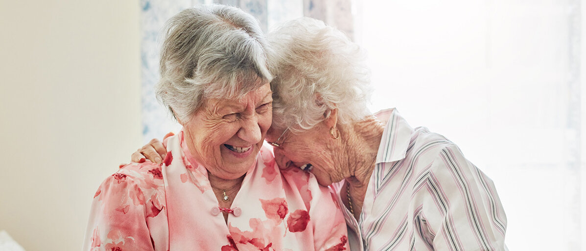 Zwei lachende Seniorinnen liegen sich im Arm