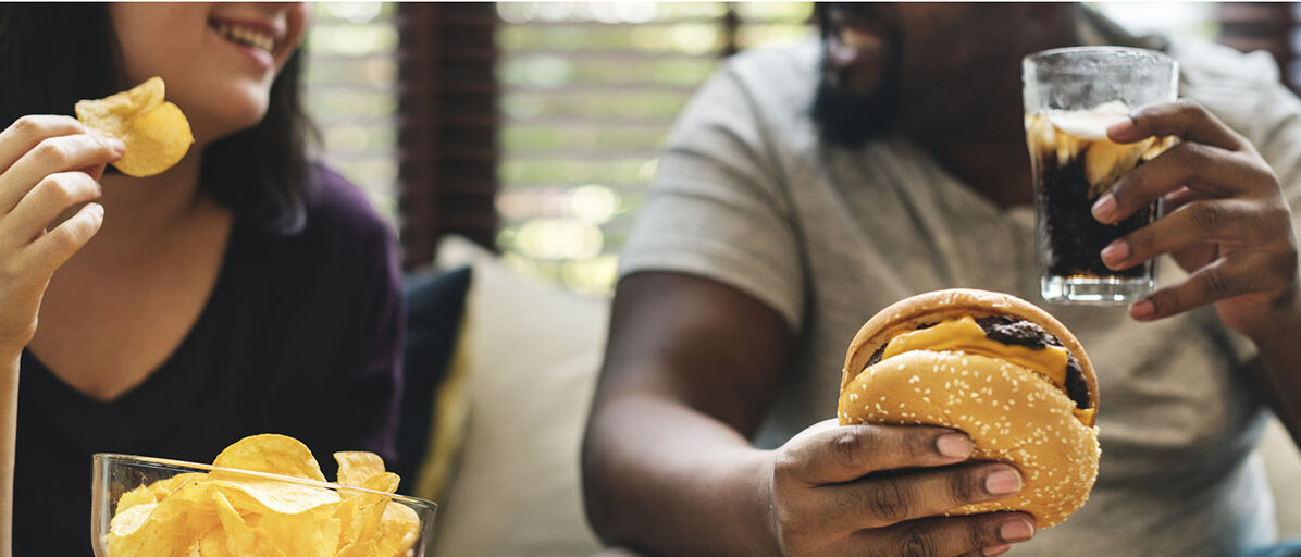 Partnerwahl und Ernährung Paar isst Burger und Chips auf der Couch