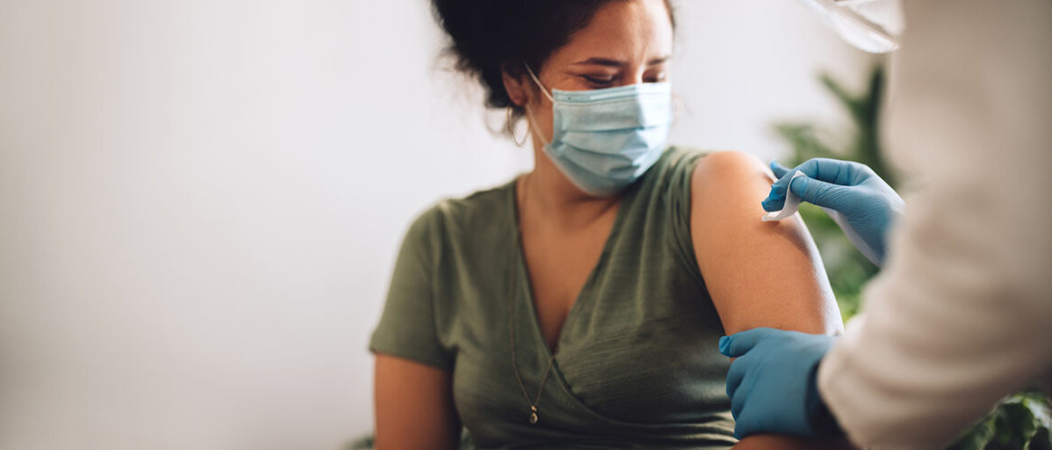 Frau mit Gesichtsmaske bekommt eine Impfung verabreicht