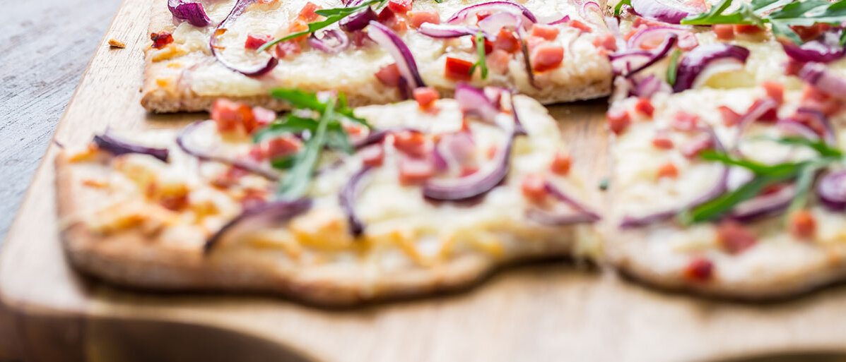 Flammkuchen selber machen Nahaufnahme eines klassischen Flammkuchens auf Holzbrett