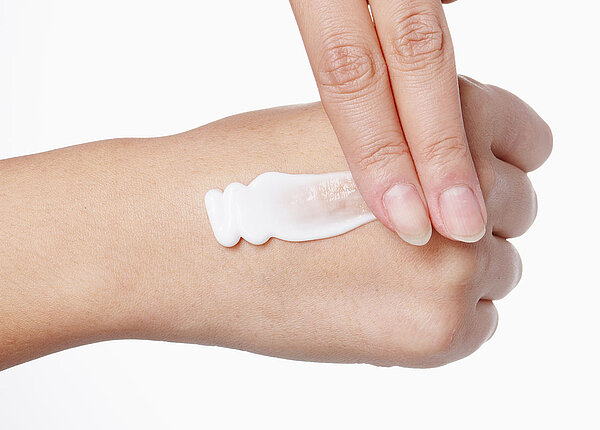 Narbenpflege für eine bessere Wundheilung Zwei Finger reiben eine Creme auf der anderen Hand ein.