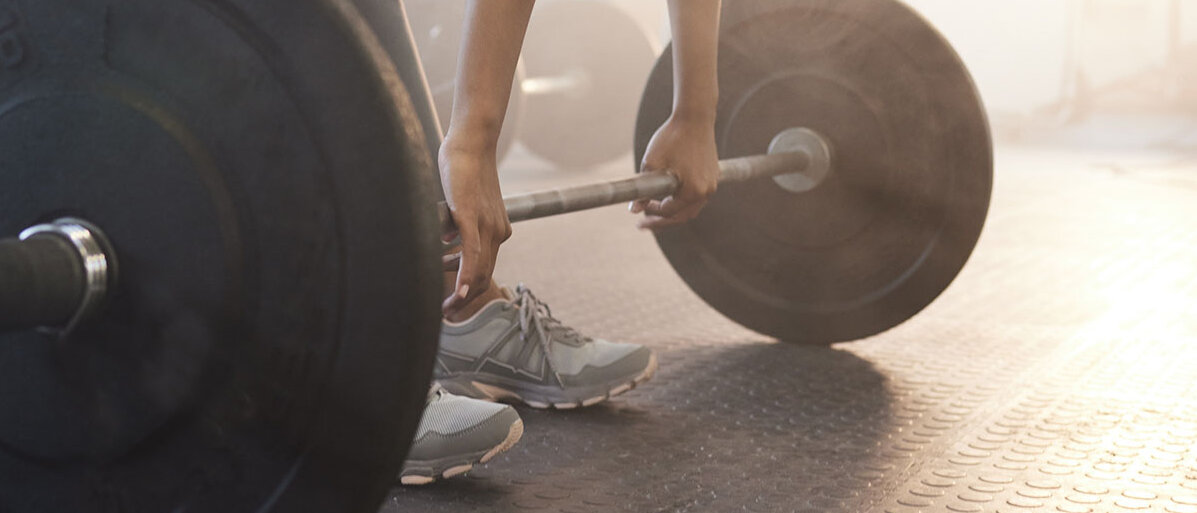 Frau stemmt Langhantel mit Fokus auf den Füßen