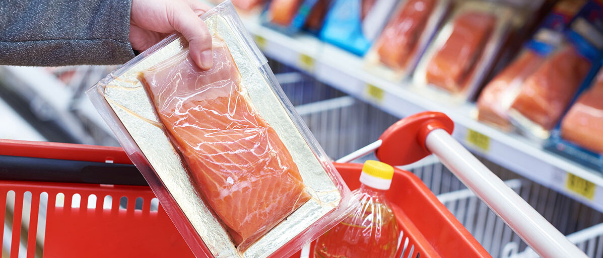 Nachhaltiger Fisch Frau legt Packung mit Lachs in ihren Supermarktwagen