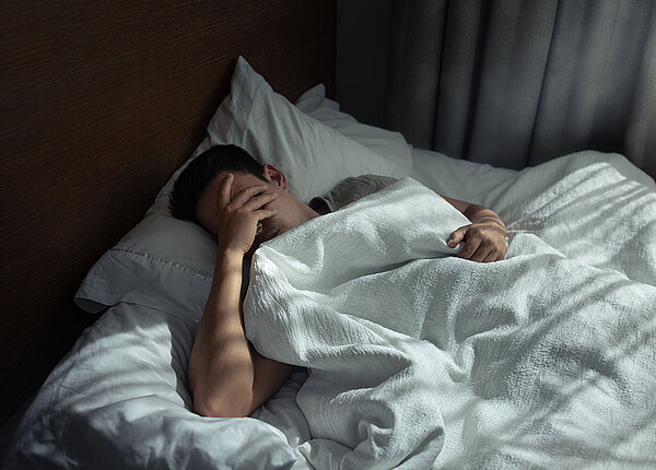 Schlafprobleme Schlafloser Mann hält sich in Bett Hand vors Gesicht