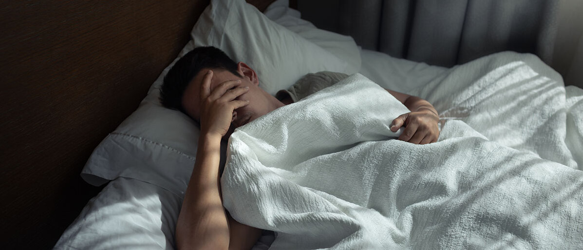 Schlafloser Mann hält sich in Bett Hand vors Gesicht
