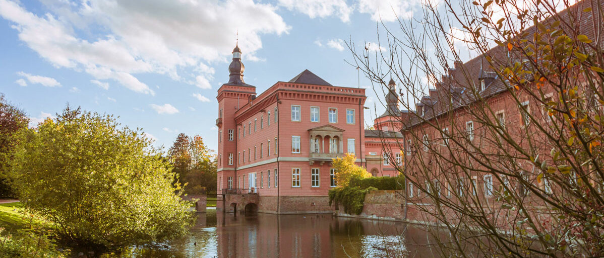 Zwei Gebäudeteile von Schloss Gracht spiegeln sich in der sie umgebenden Wasseranlage.