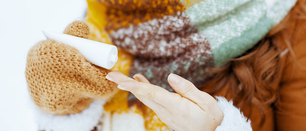 Lächelnde Frau cremt sich draußen im Freien die Hände ein