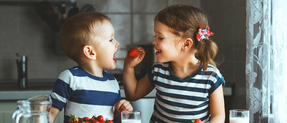 Geschwister essen zusammen Erdbeeren in der Kueche