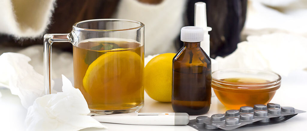 Frau presst Zitrone in Tasse aus, daneben Erkältungsmedikamente und ein Fieberthermometer 