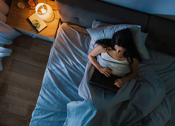 Junge Frau sitzt im Bett und arbeitet an einem Laptop in der Nacht.