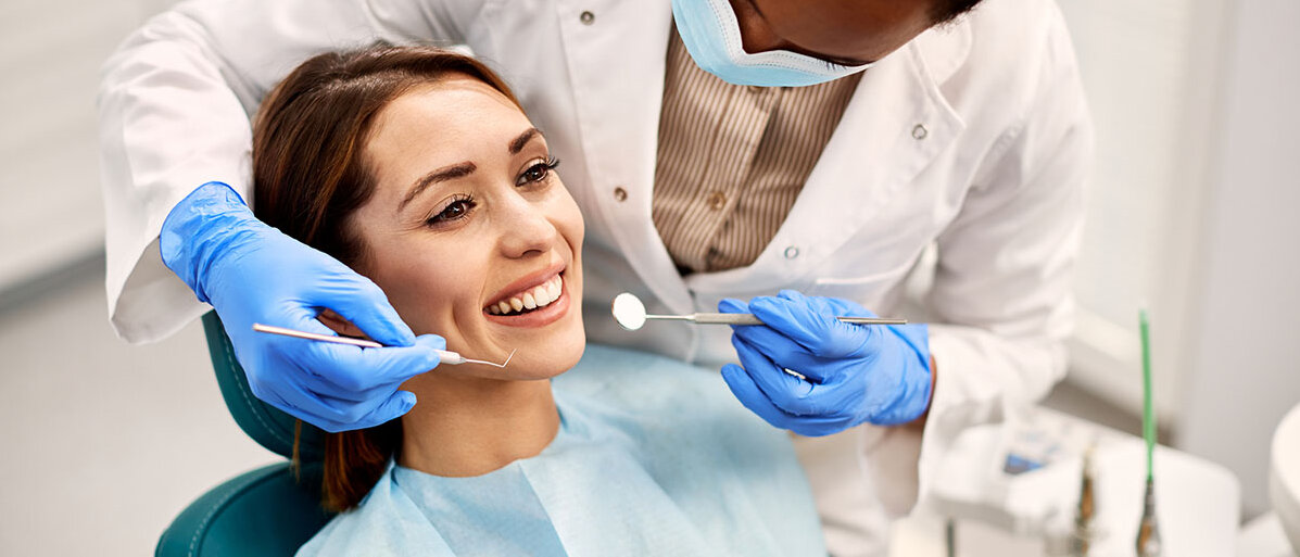 Hilfe bei lockeren Zähnen Junge Frau sitzt beim Zahnarzt auf dem Behandlungsstuhl und lächelt während Zahnärztin ihre Zähne begutachtet.