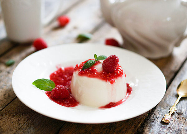 Panna Cotta mit Himbeersauce und Minze auf einem weißen Teller