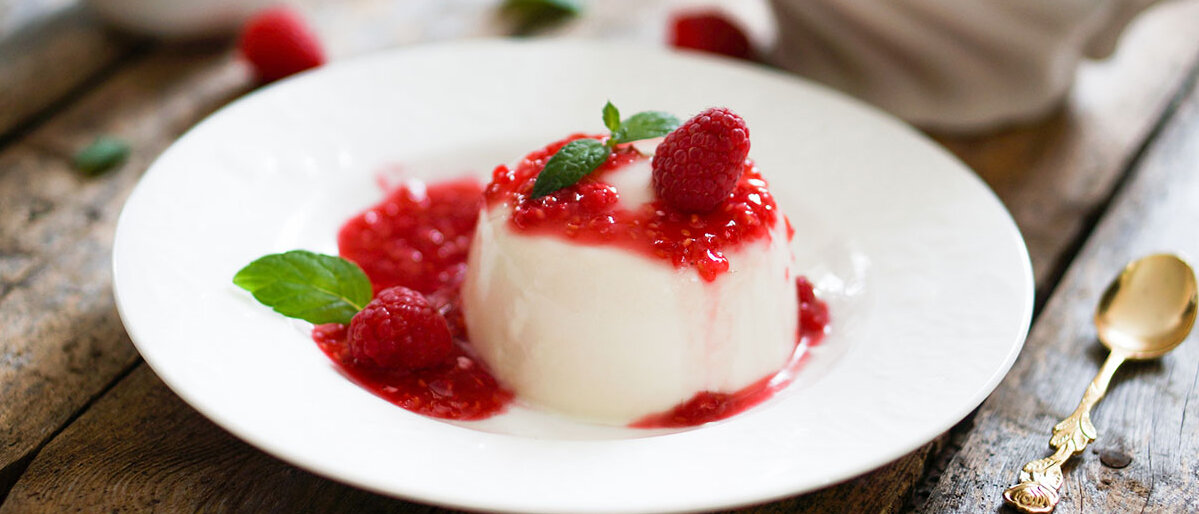 Panna Cotta mit Himbeersauce und Minze auf einem weißen Teller