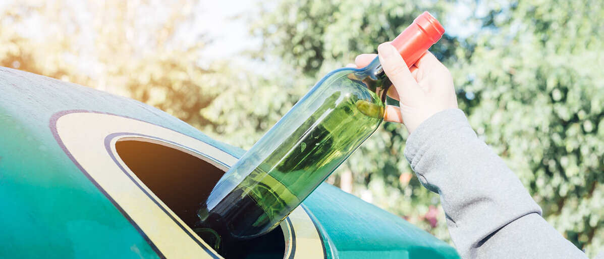Hand wirft eine Flasche Wein in einen Glascontainer