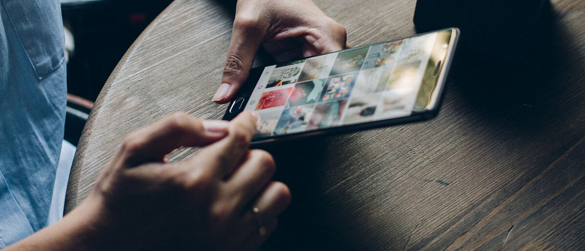 Mann hält Handy in Hand. Eine Social Media Plattform ist geöffnet.