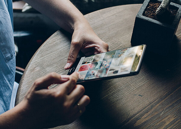 Mann hält Handy in Hand. Eine Social Media Plattform ist geöffnet.