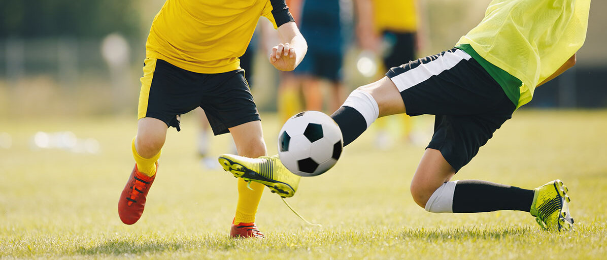 Sportverletzung am Knie Text: Zwei Fußballer in gelben Trikots kämpfen um den Ball