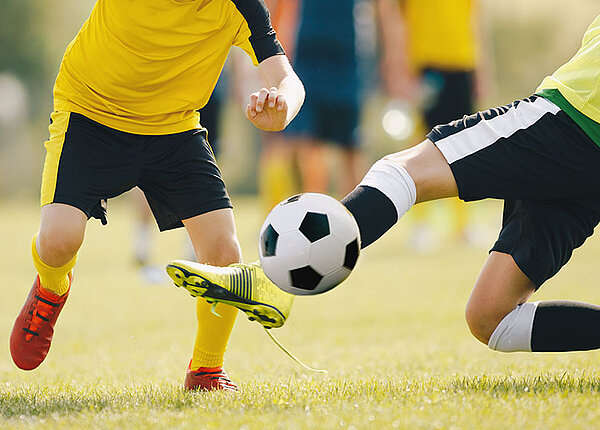 Text: Zwei Fußballer in gelben Trikots kämpfen um den Ball 