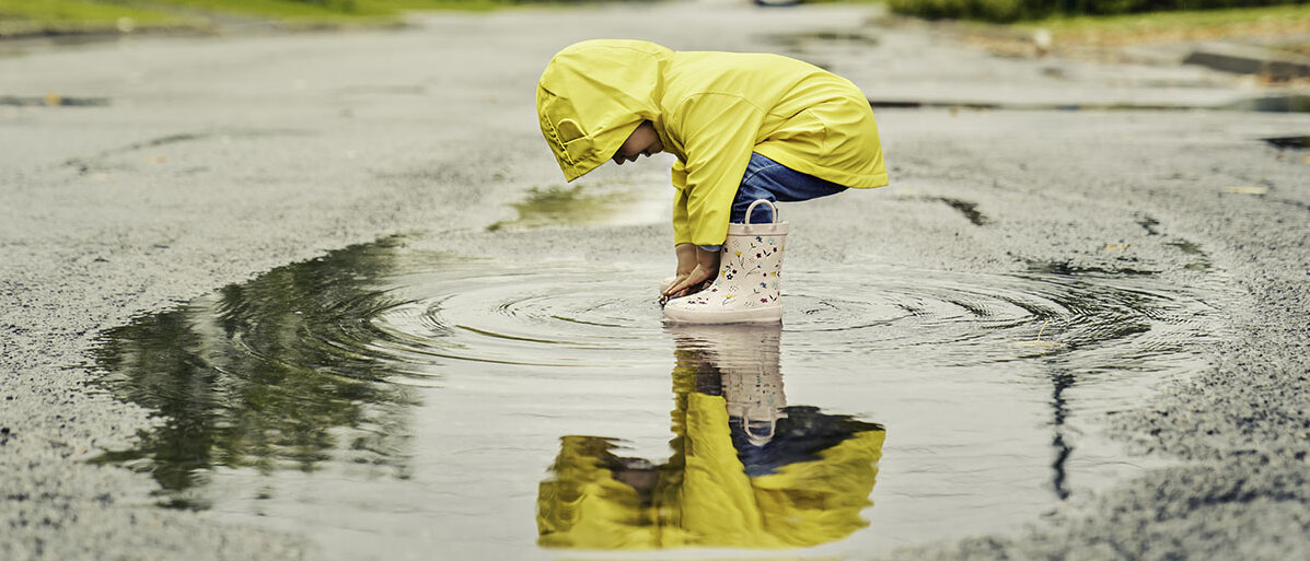 Mädchen mit gelber Regenjacke steht in einer Wasserpfütze