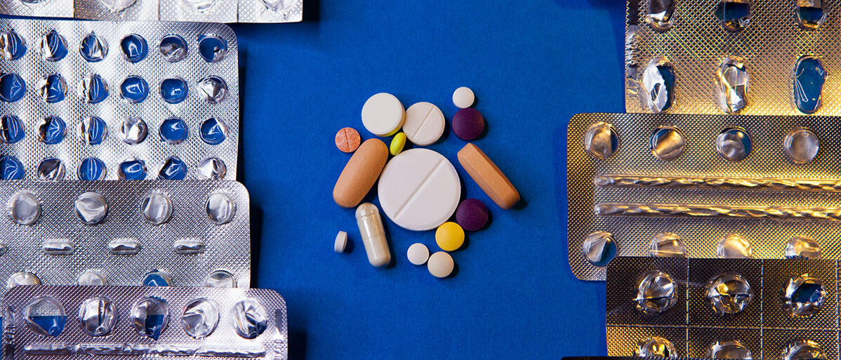 Am Bildrand liegen mehrere verschiedene leere Arzneimittelblister. In der Mitte liegen in einem Kreis verschiedene Tabletten und Kapseln.