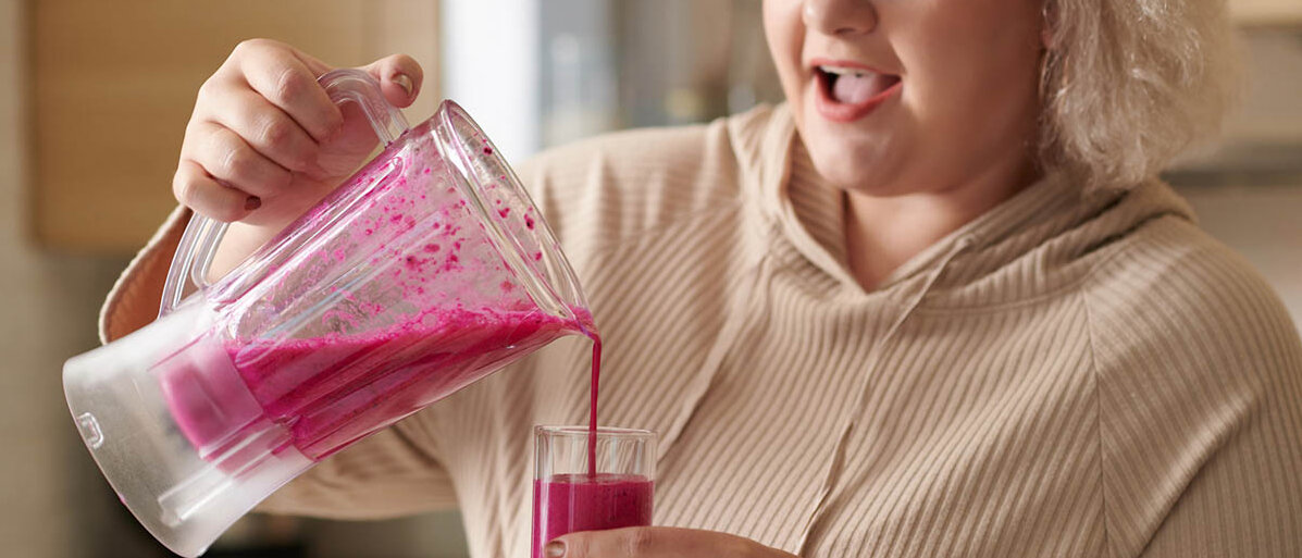 Eine Frau gießt sich einen knallpinken Smoothie aus dem Mixer in ihr Trinkglas.