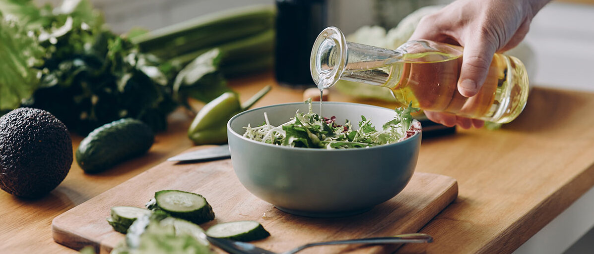 Mann gibt Olivenöl aus Flasche über grünen Salat