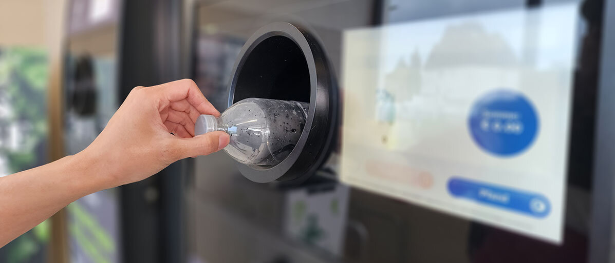 Frau steckt Pfandflasche in Automaten.