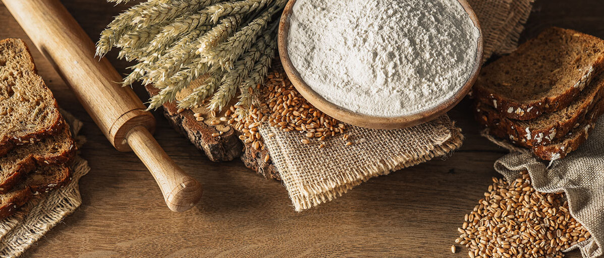 Brot, Getreide, Ähren und Mehl auf einem dunklen Holzgrund