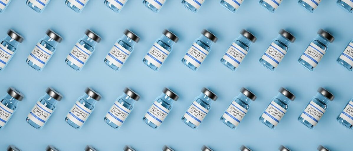 Viele Flaschen mit Corona-Impfstoff auf blauem Untergrund.