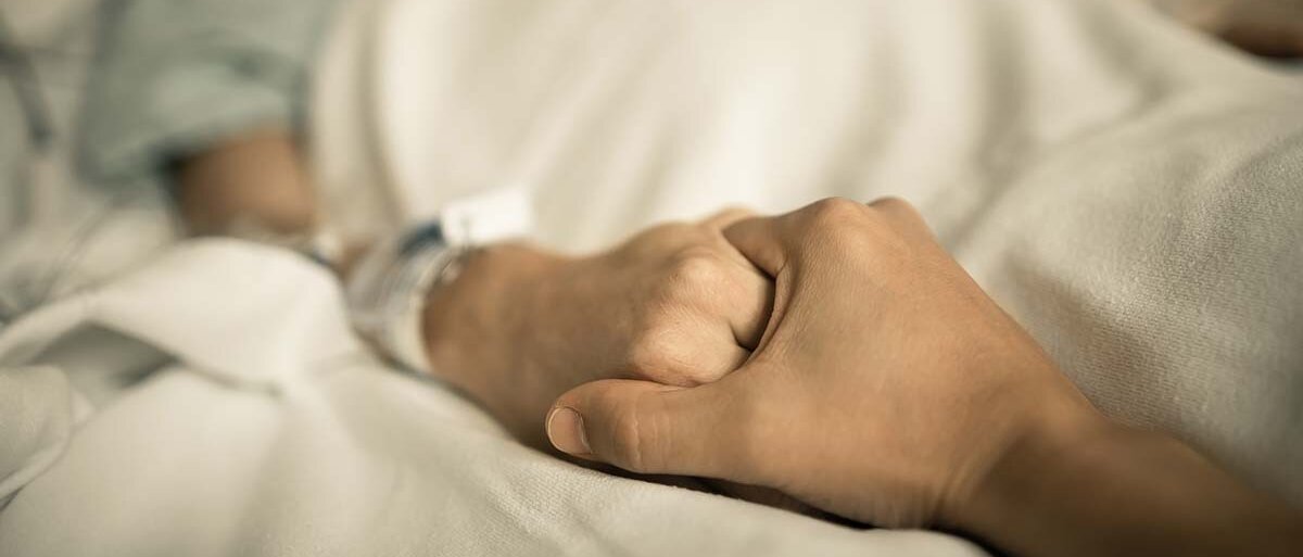 Jemand hält die Hand einer Person, die in einem Krankenhausbett liegt