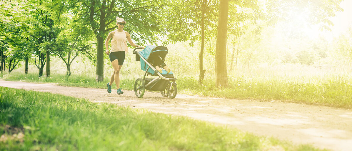 Joggen mit Kinderwagen Frau joggt mit Kinderwagen über Waldweg