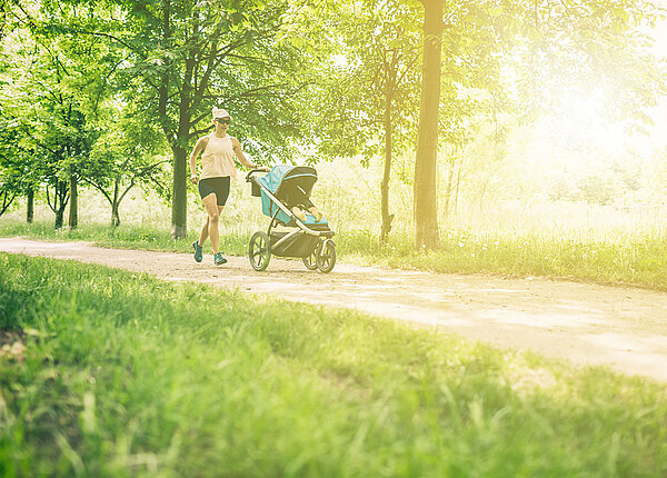 Joggen mit Kinderwagen Frau joggt mit Kinderwagen über Waldweg