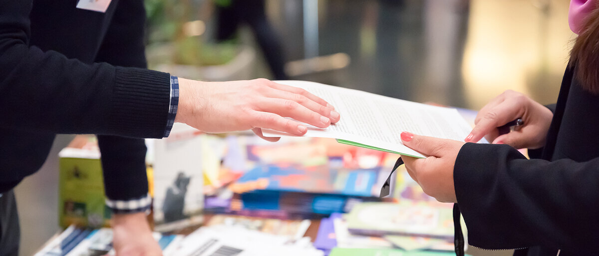 Jemand überreicht einer anderen Person Broschüren
