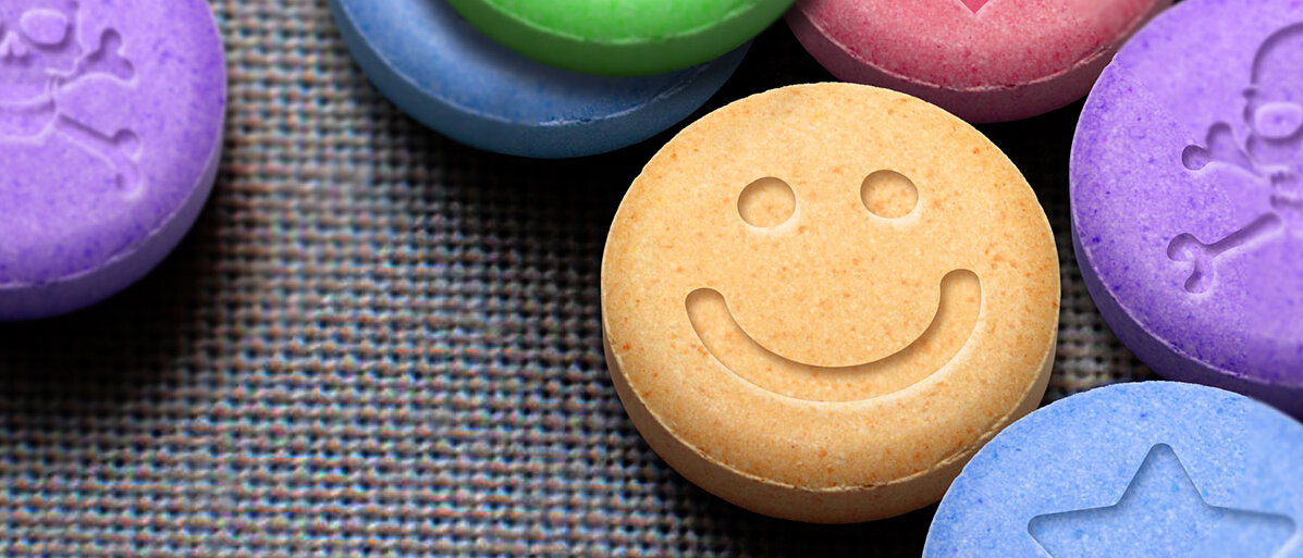 Mehrere bunte runde Tabletten mit verschiedenen Motivprägungen, im Fokus steht eine gelbe Tablette mit einem Smiley.