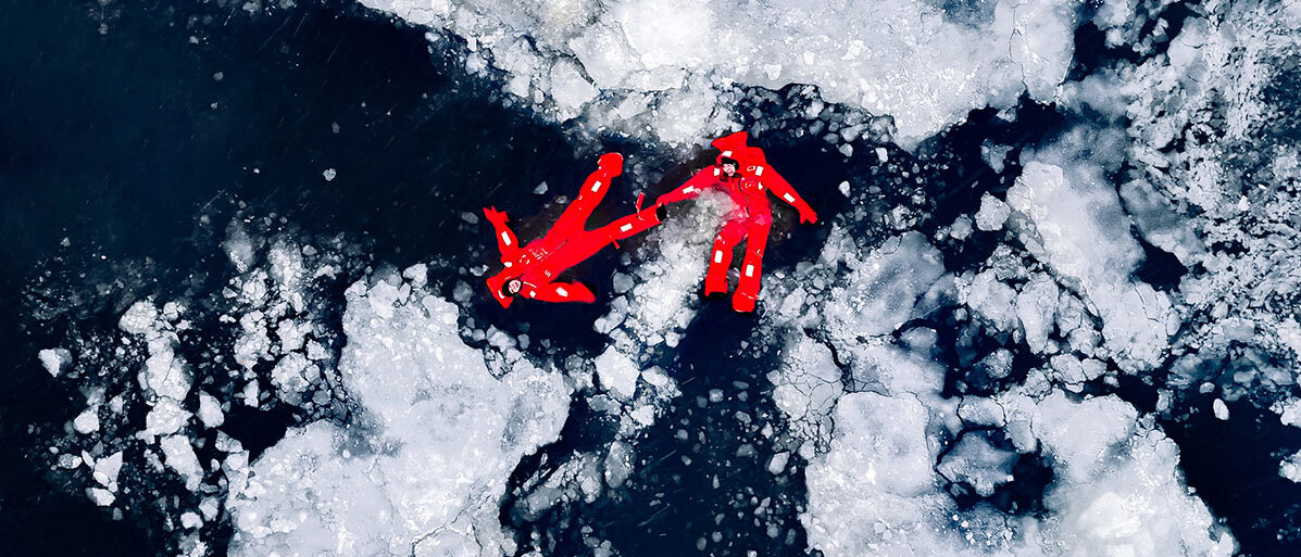 Zwei Personen in roten Survival-Anzügen liegen auf der Wasseroberfläche des arktischen Meers.