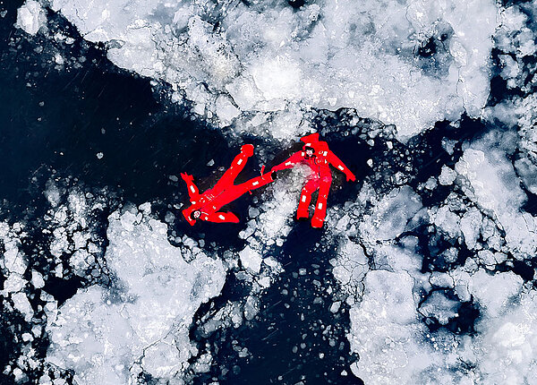 Erste Hilfe bei Unterkühlung: Maßnahmen, um Erfrierungen zu behandeln Zwei Personen in roten Survival-Anzügen liegen auf der Wasseroberfläche des arktischen Meers.