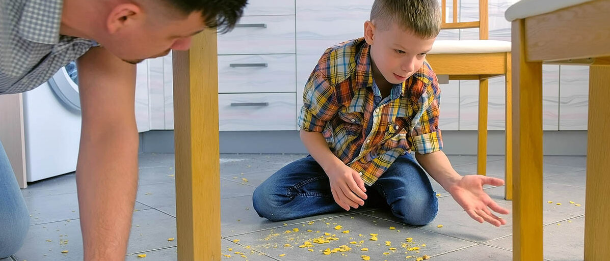 Vater und Sohn unter dem Küchentisch: Der Sohn hat Cornflakes verschüttet. Beide räumen gemeinsam auf.