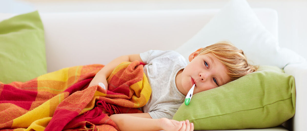 Gefährliches Fieber bei Kindern erkennen Kranker kleiner Junge liegt mit Fieberthermometer im Mund auf der Couch.