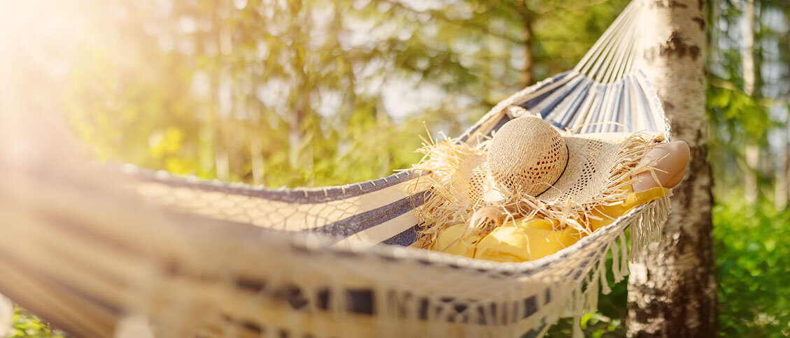 Verantwortung auch mal abgeben und entspannen Frau in Hängematte. Ihr Gesicht ist mit einem Strohut bedeckt.