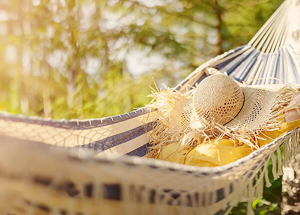 Frau in Hängematte. Ihr Gesicht ist mit einem Strohut bedeckt.